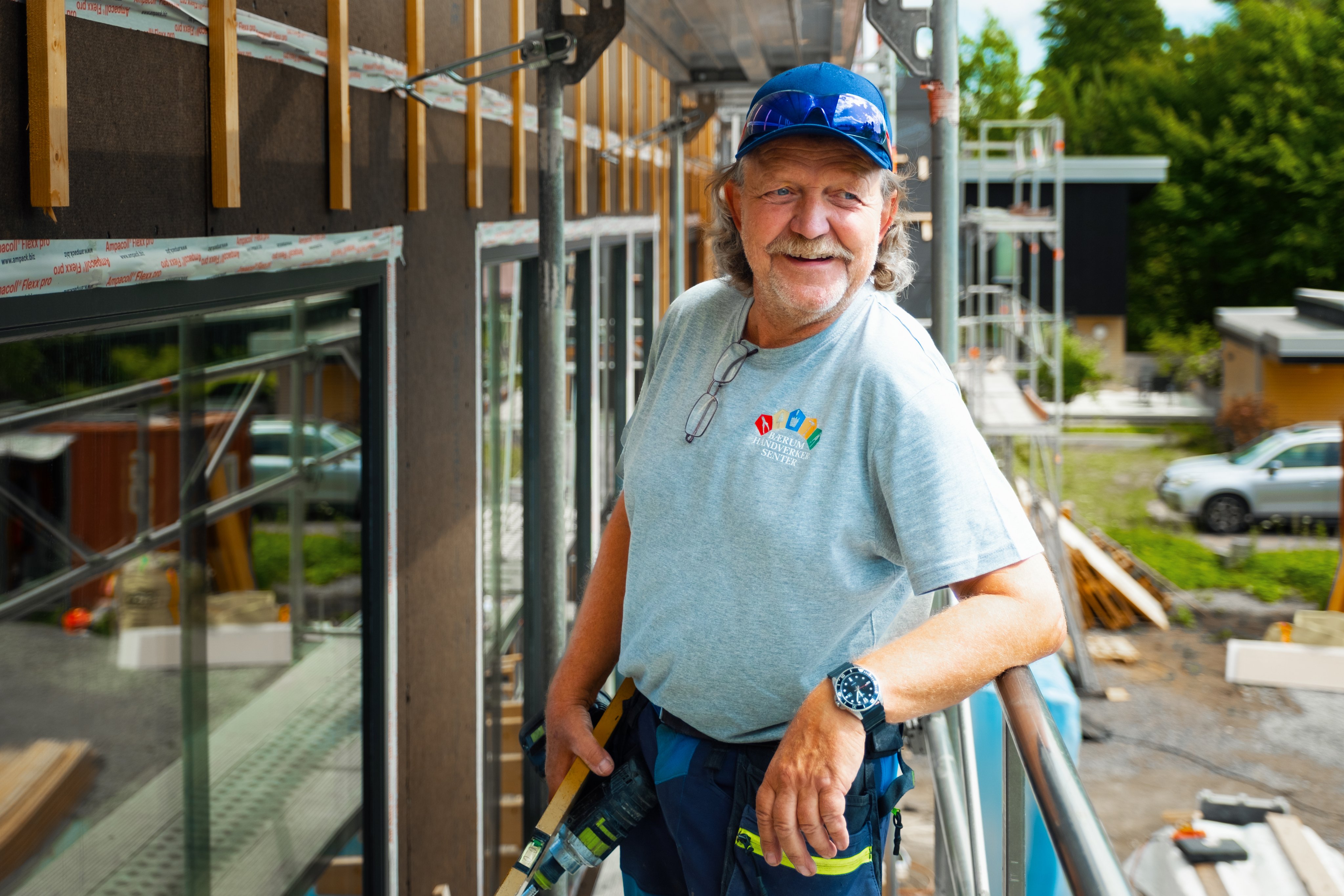 En snekker som står på en stilas foran et hus under oppbygging.