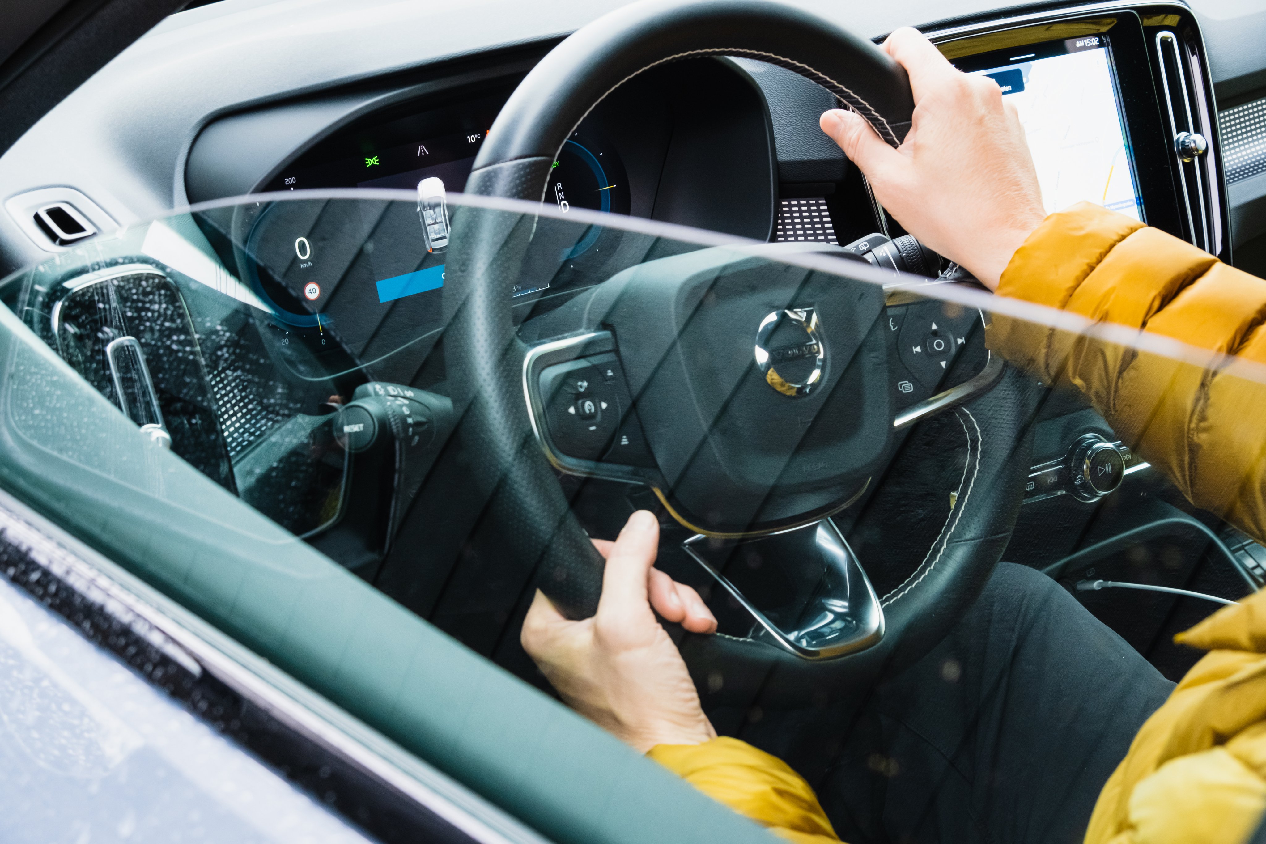 Nærbilde av rattet på en bil, sett utenfra vinduet på førersiden. Sjåfør sitter i førersetet og holder i rattet.