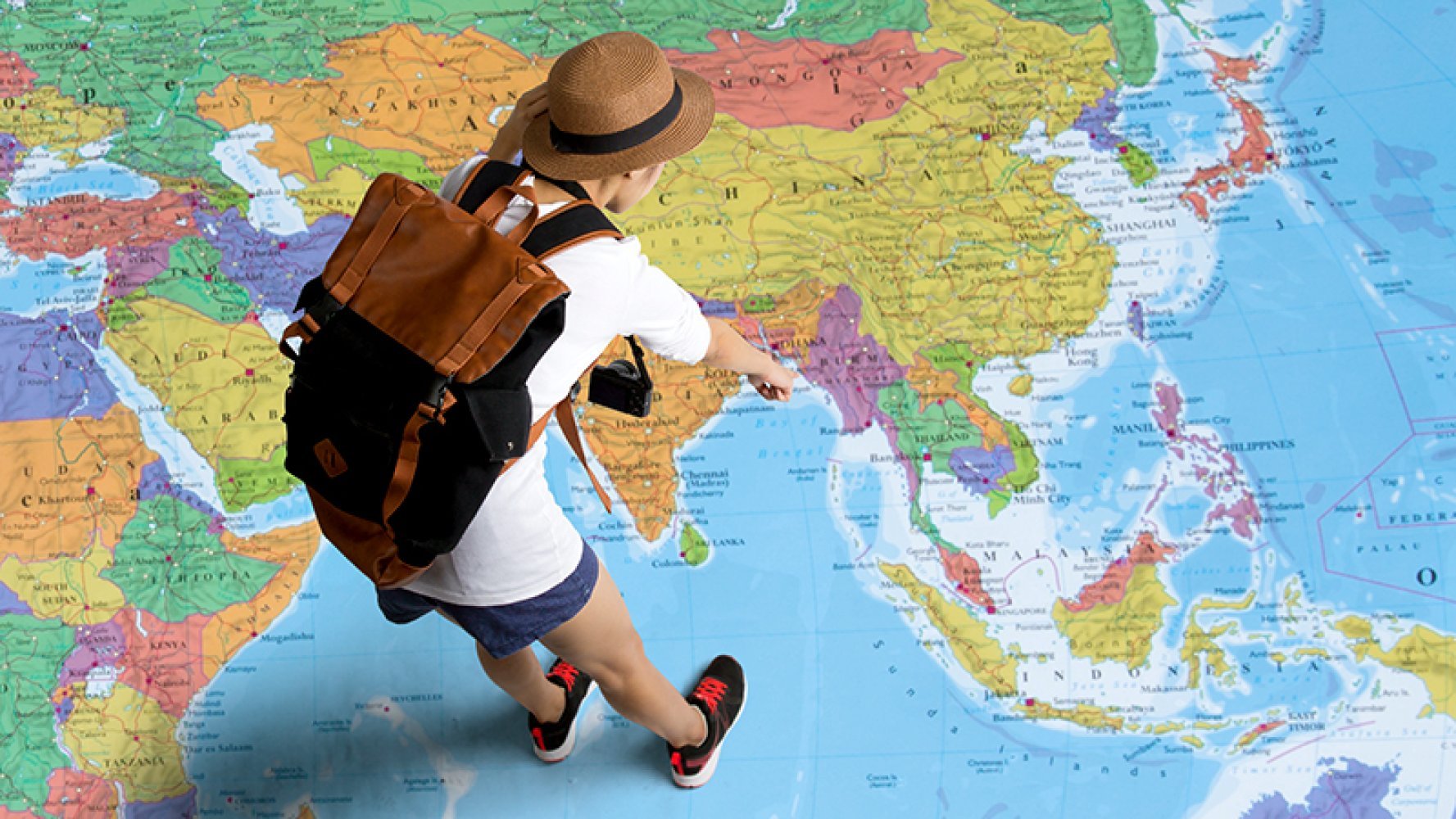 Person med sekk på ryggen står på et gigantisk verdenskart og peker ned på på kartet.