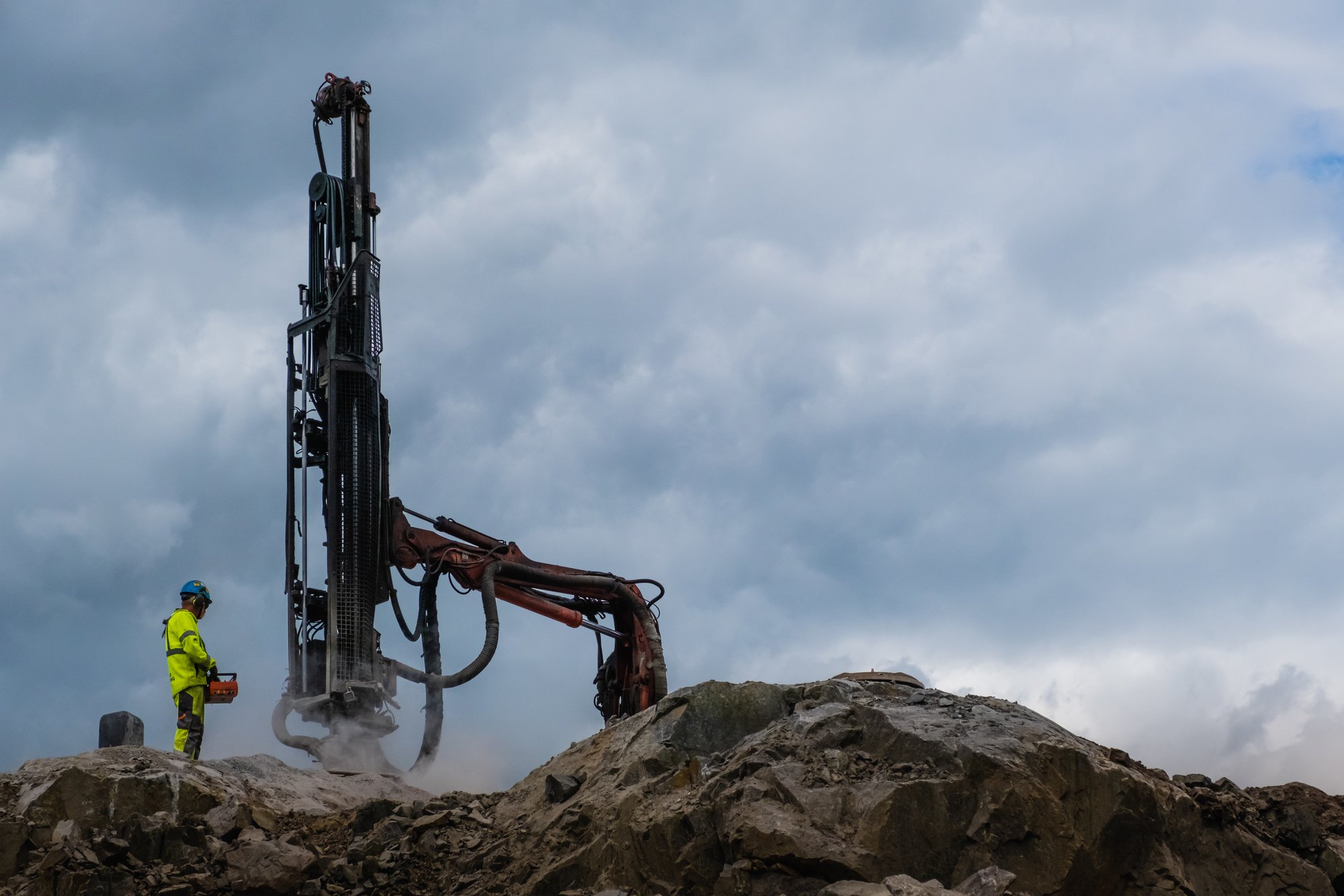Anleggsarbeider i refleksklær styrer en stor boremaskin på en steinfylling.