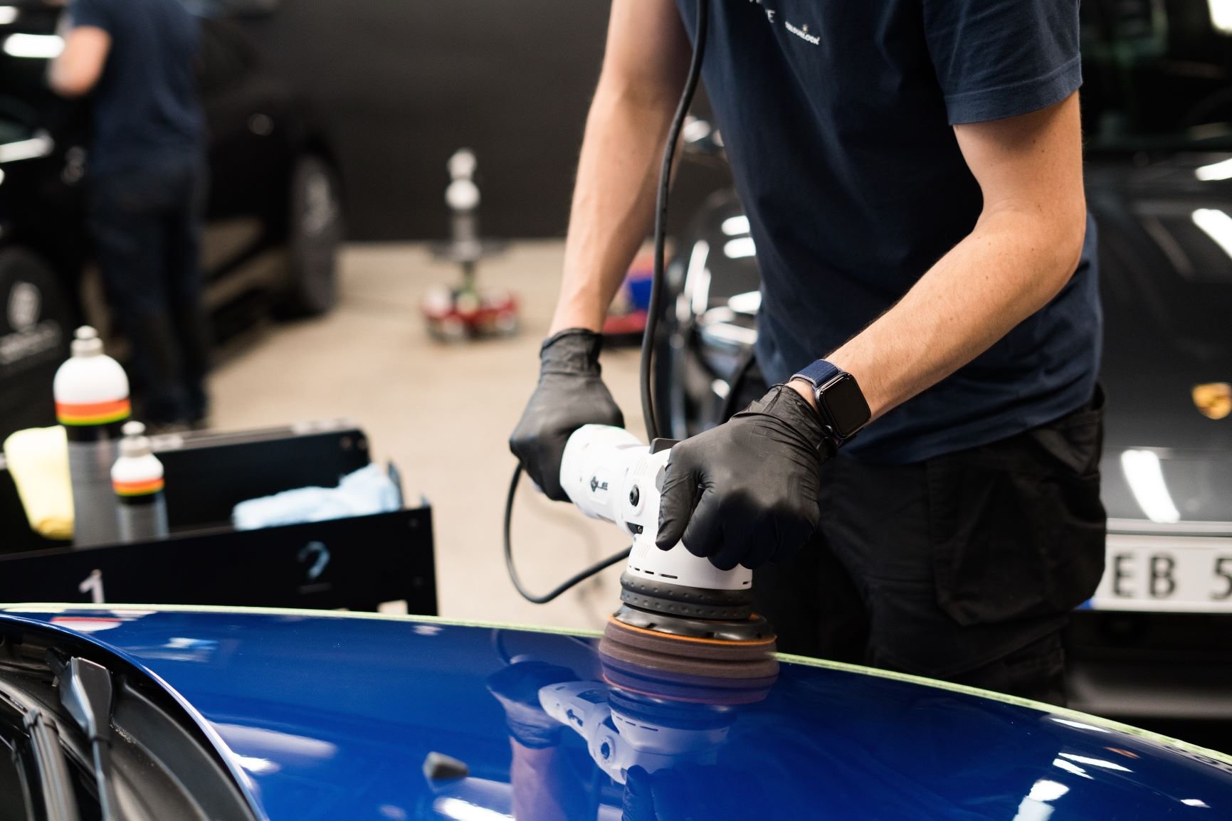 To armer som polerer et blått bilpanser med en maskin