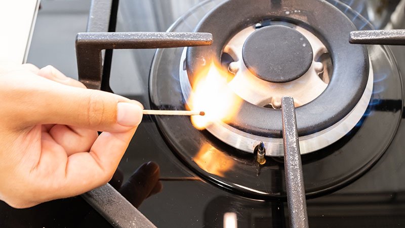 Hånd som holder en tent fyrstikk over en stekeplate drevet av propangrass