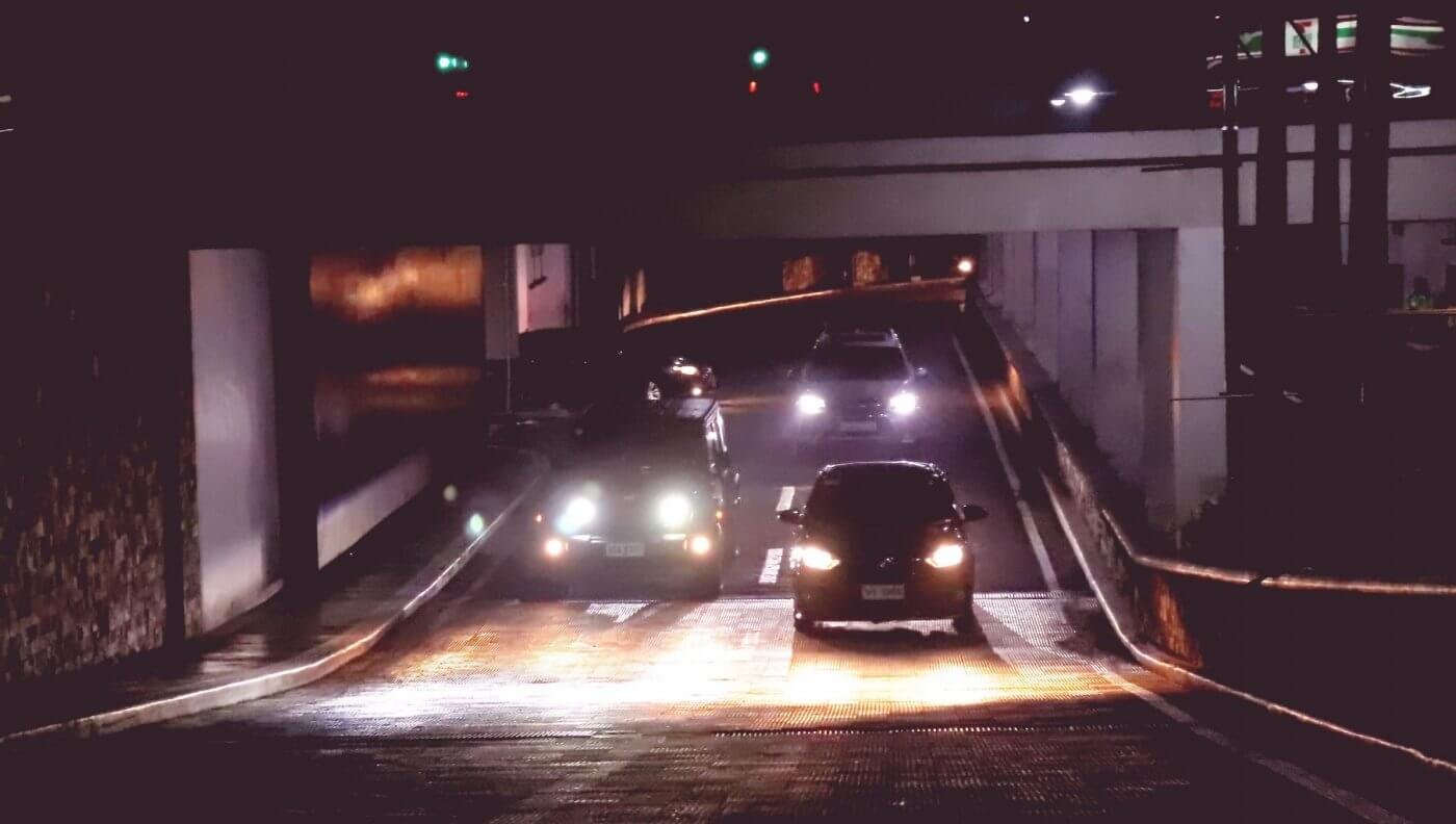 Flere biler sett forfra på en mørk vei, med frontlyktene på. 