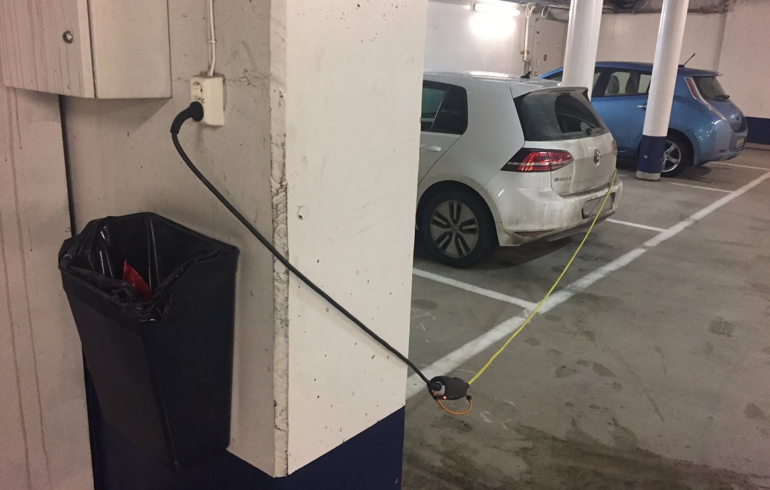 Bil parkert i parkeringshus lades ved hjelp av en lang ledning koblet til vanlig kontakt.