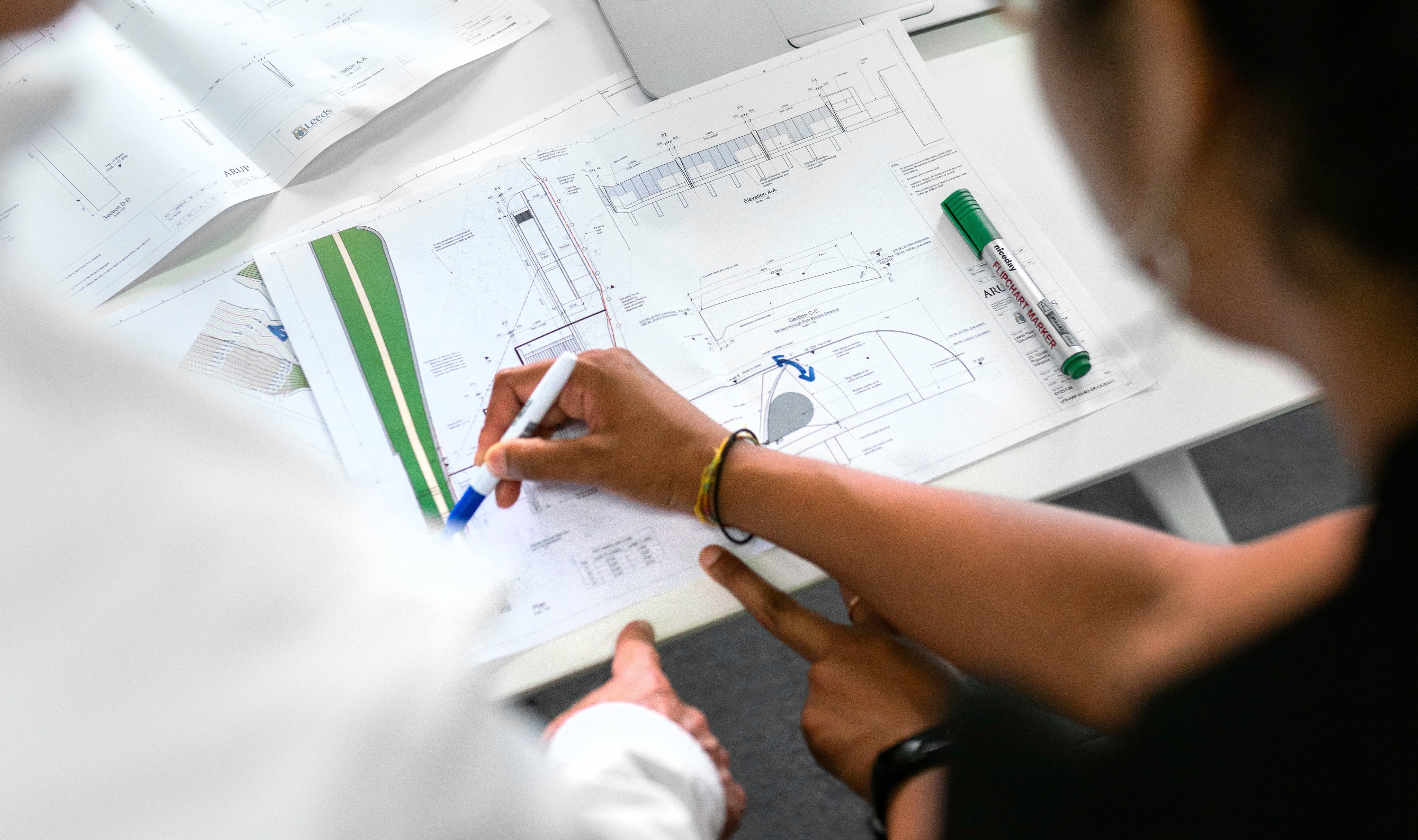 Hender som peker og markerer på ark med ingeniørtegninger.