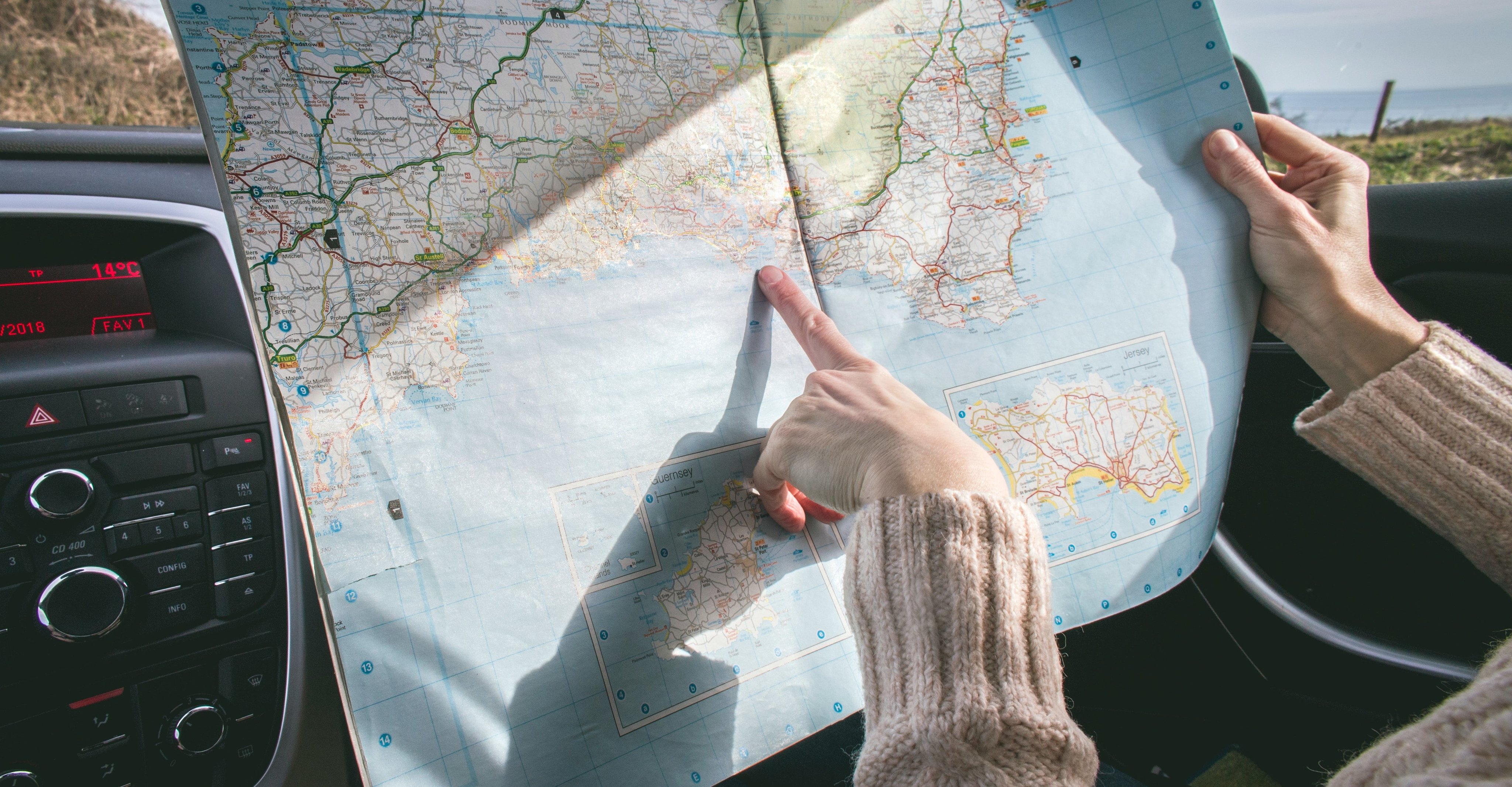 Kart som holdes av en person i passasjersetet i en bil, vedkommende peker på et sted i kartet