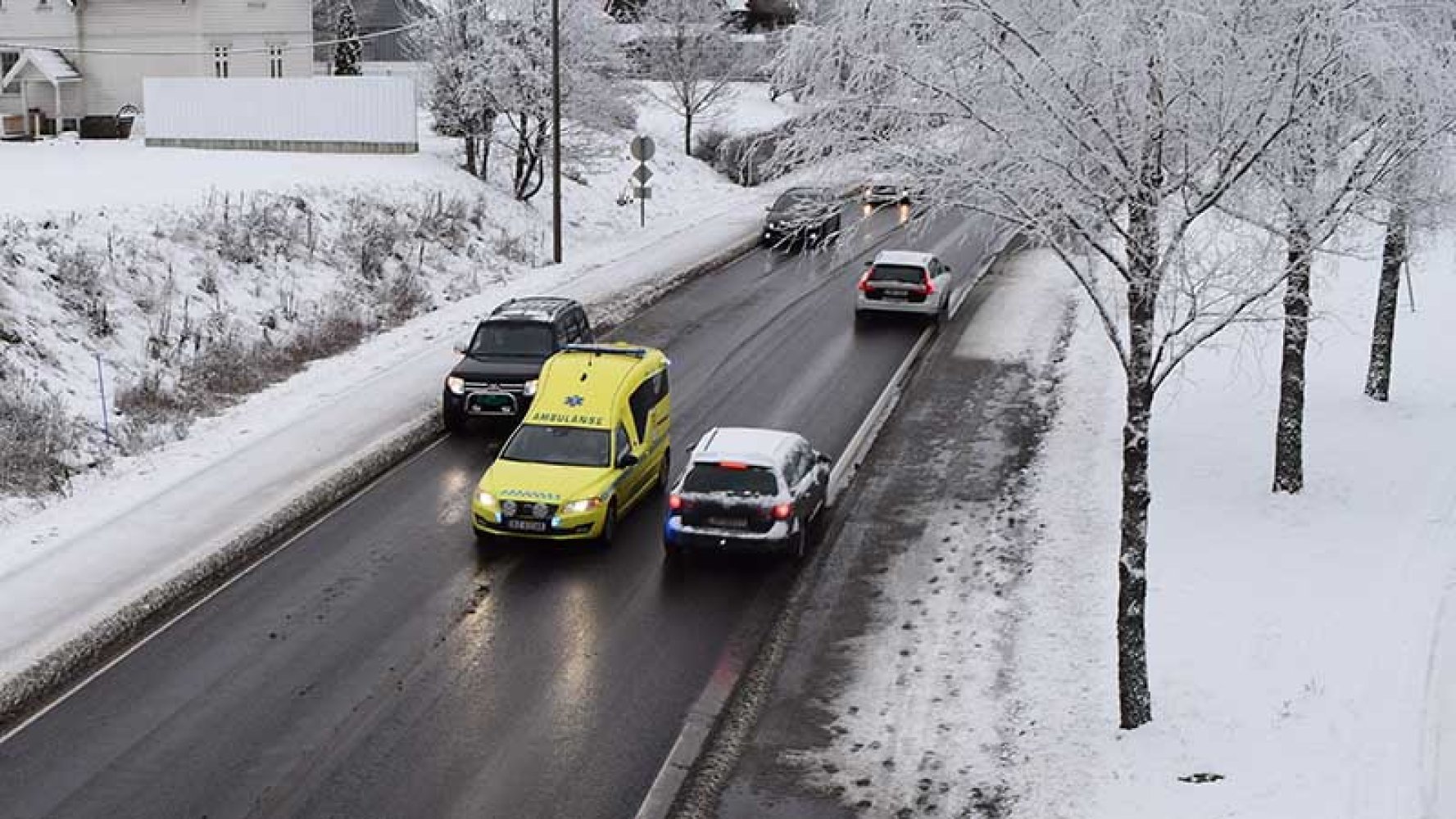 Ambulanse og politikjøretøy kjører på en vintervei med snø langs veikanten.