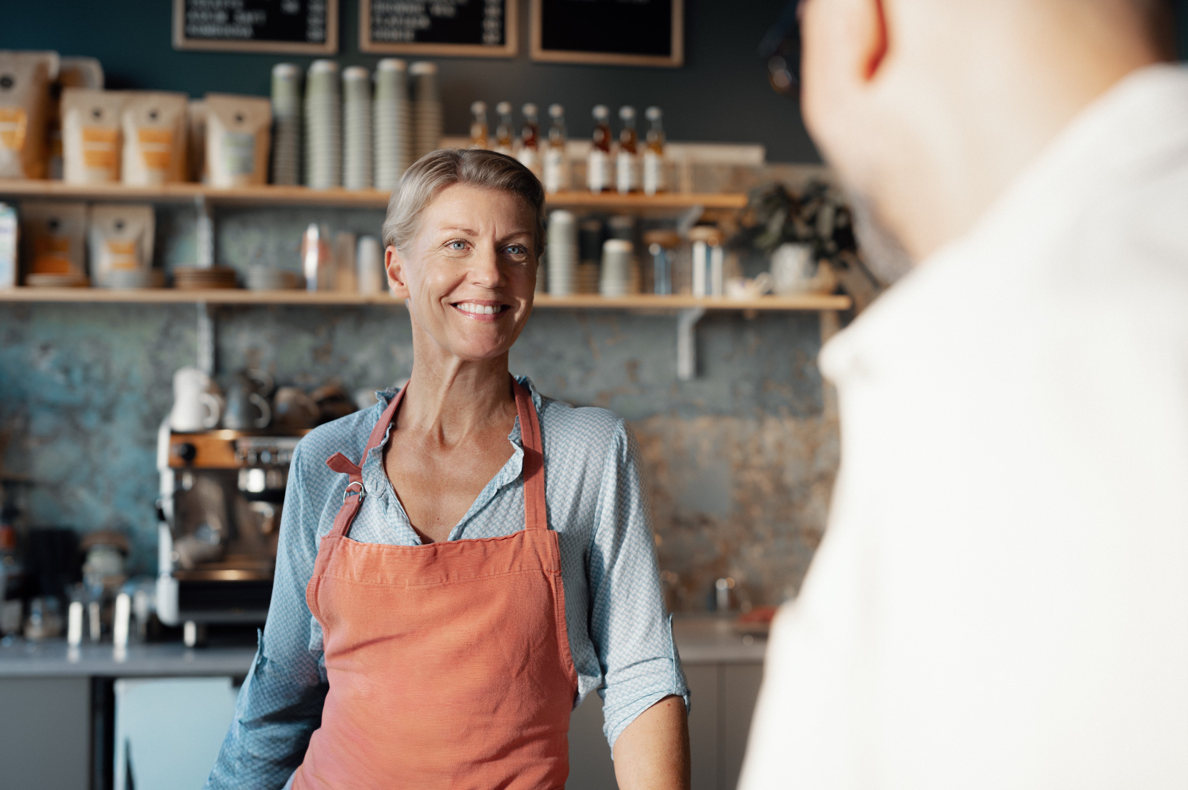 Eier av en kafé som smiler til en kunde bak disken.