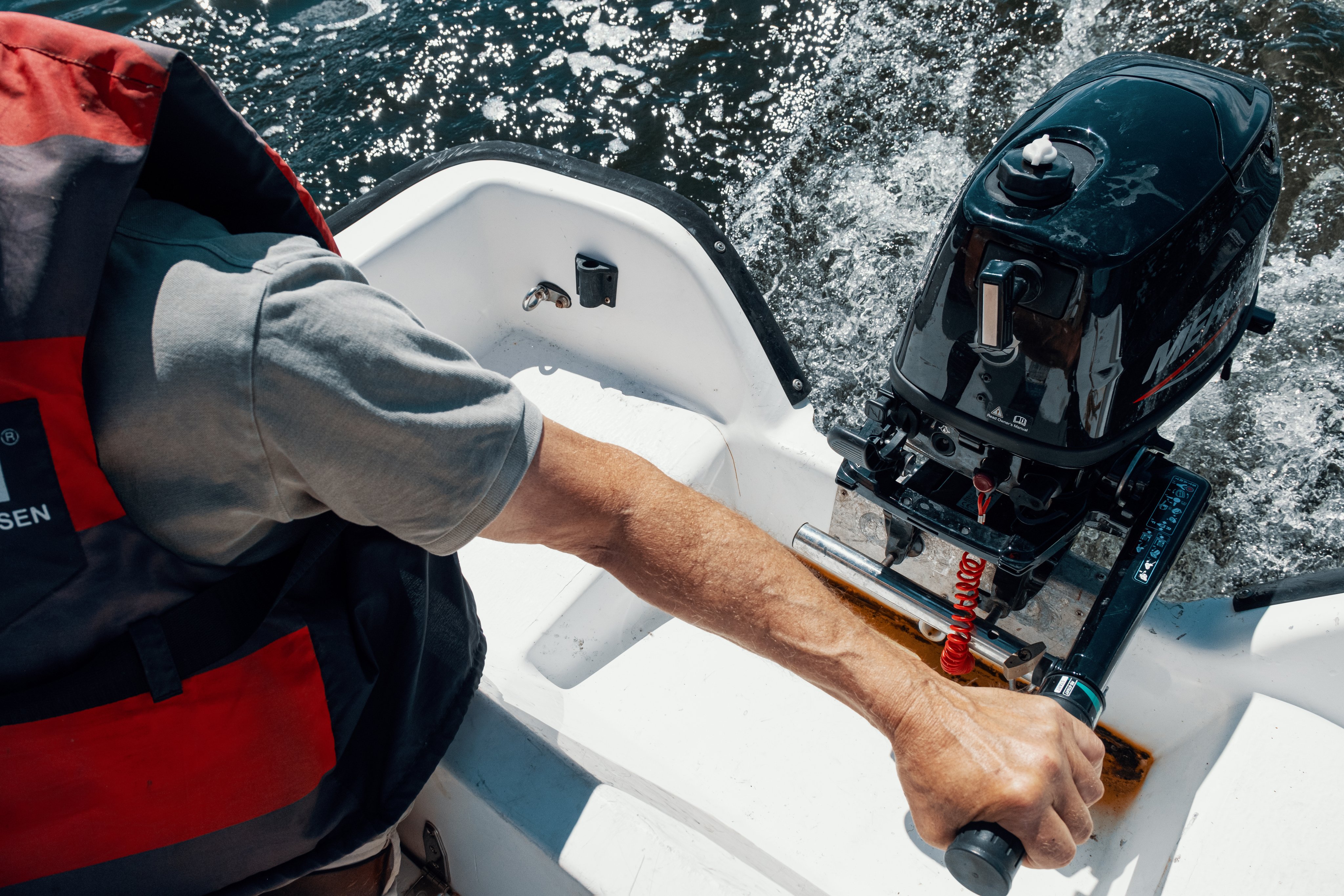 En person styrer en påhengsmotor på en liten båt mens vannet spruter bak.