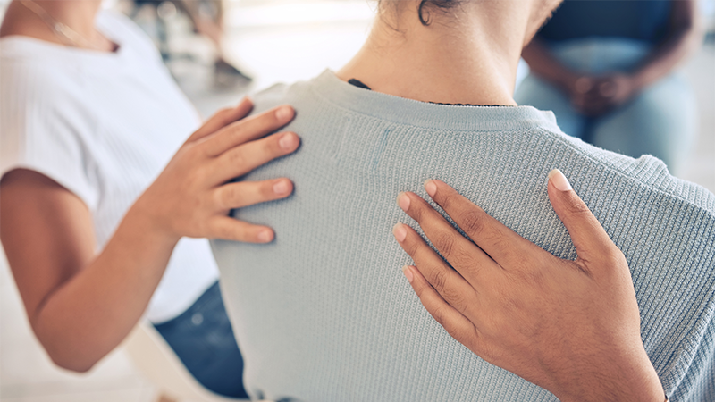 To personer legger hendene sine på en dames skuldre.