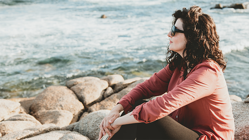 En kvinne sitter ved en sjø og ser utover landskapet.