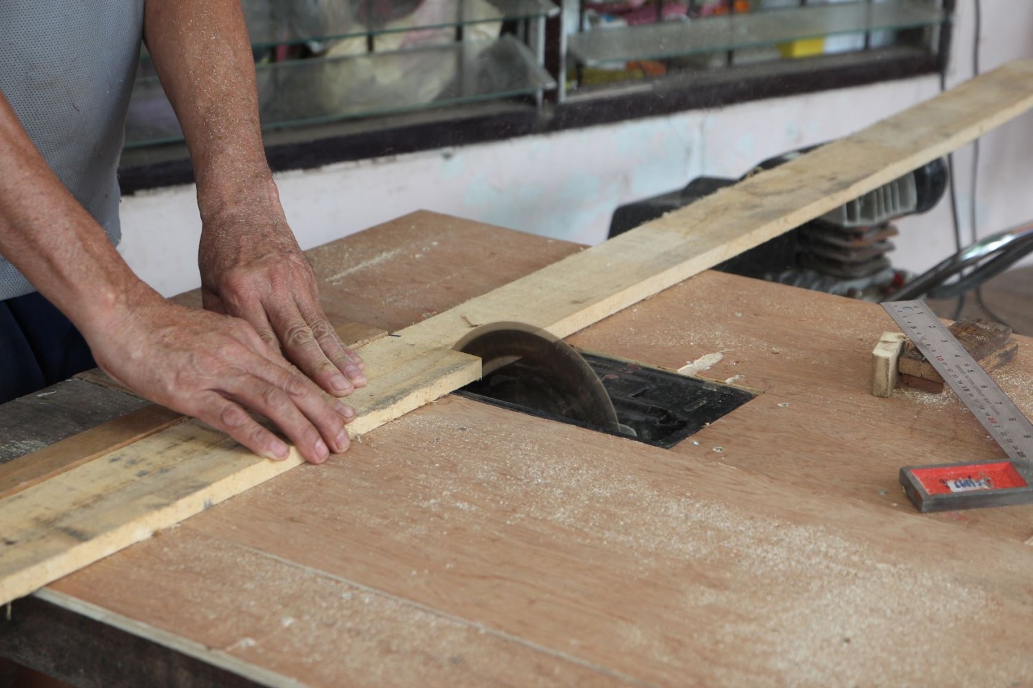 Mannlige hender som kutter en planke på en sirkelsag oppå en treplate med verktøy rundt.