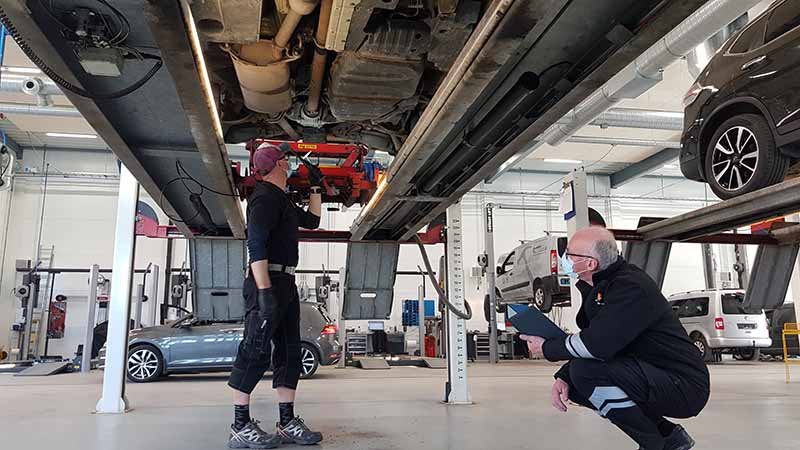 To menn ser på undersiden av en oppheiset bil.