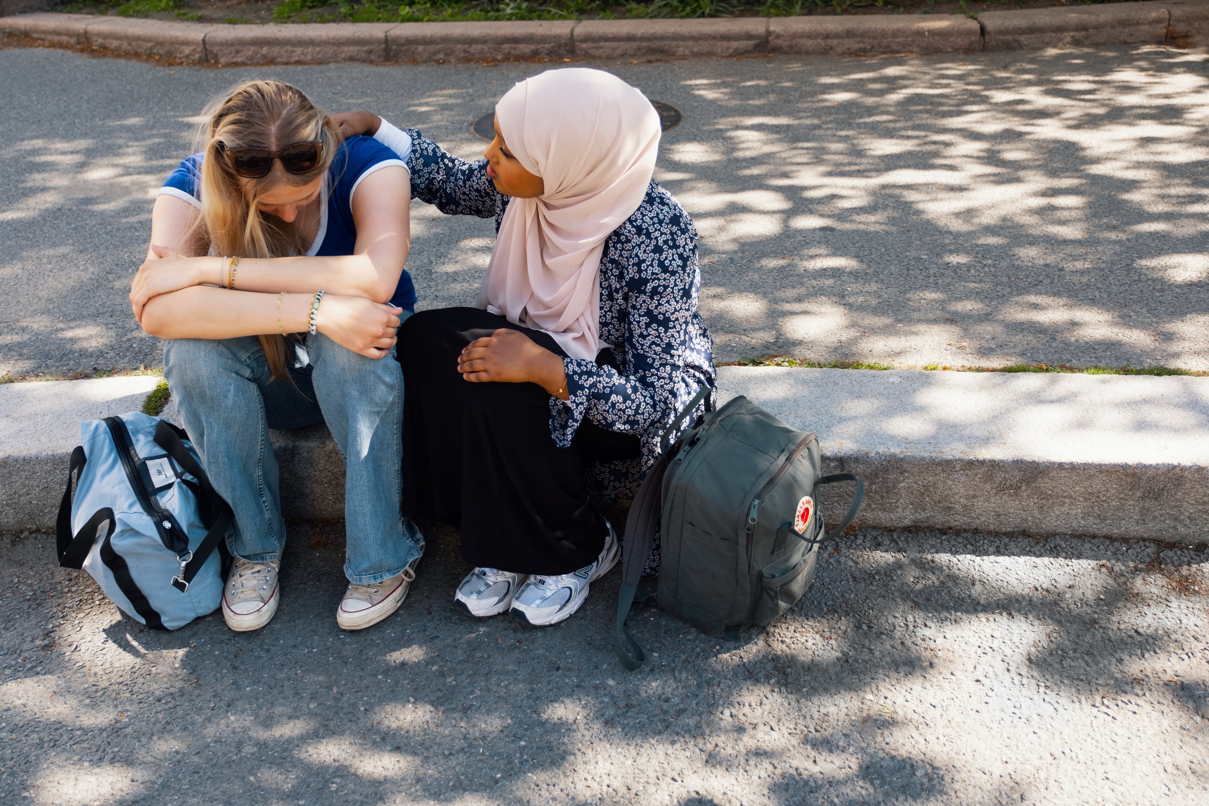 To studenter sitter på en fortauskant, den ene med armen rundt den andre.
