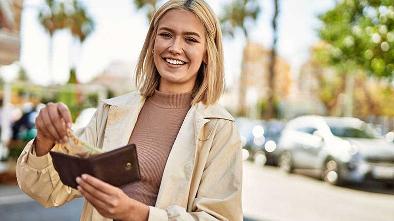 Ung kvinne smiler og tar ut en 500-lapp fra en lommebok hun holder.