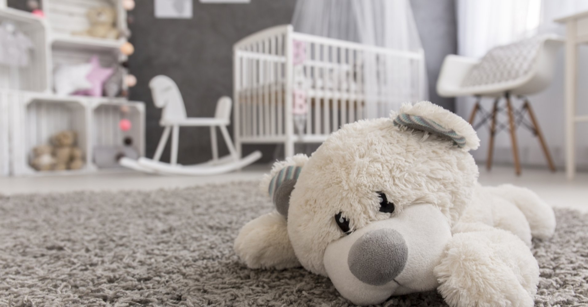 Kosedyr ligger på et teppe i et barnerom med sprinkelseng i bakgrunnen.