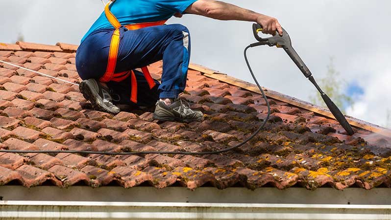 En mann rengjør et tak med høytrykksspyler.