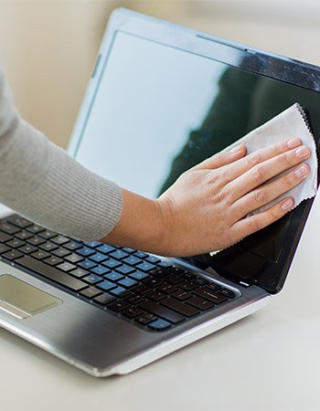 En hånd som tørker støv av skjermen på en bærbar PC.