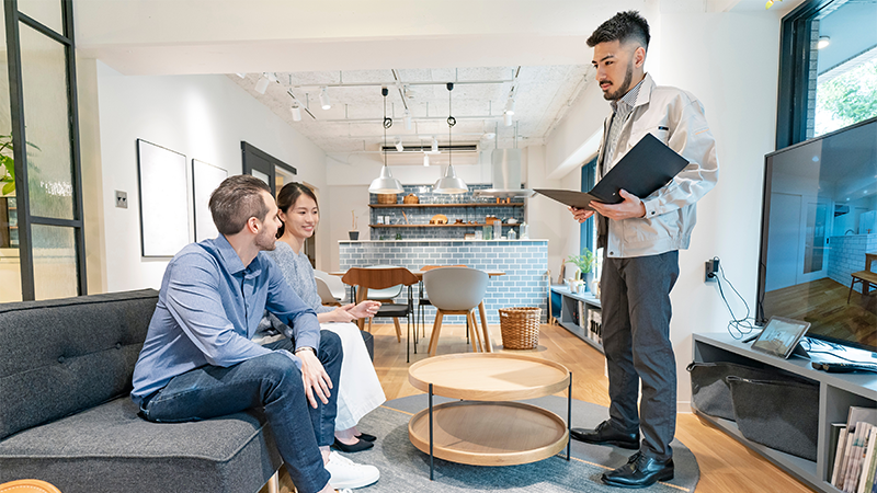 Et par sitter i sofaen og ser på en meiendomsmegler