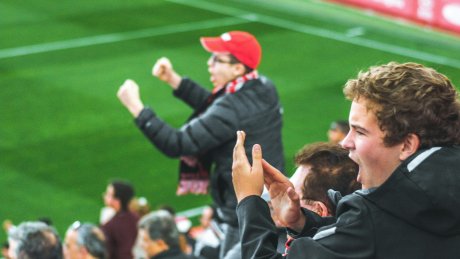 Jublende supportere på fotballtribune, med fotballbanen i bakgrunnen