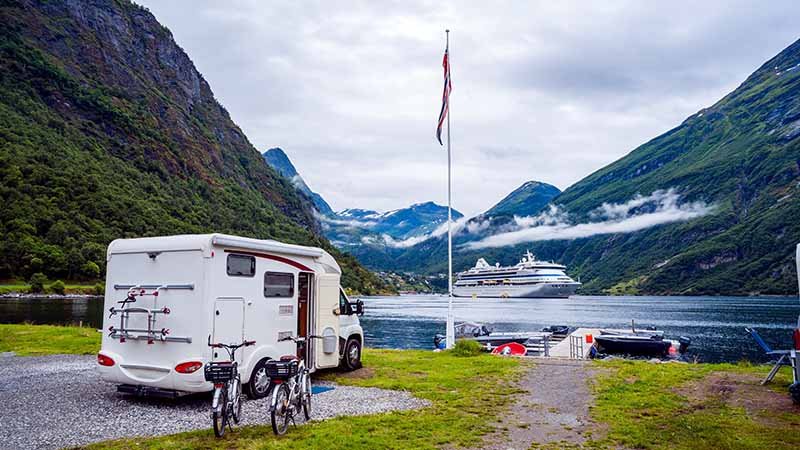 En bobil er parkert foran en fjord omgitt av fjell.