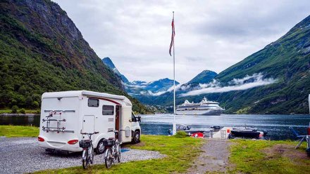 En bobil er parkert foran en fjord omgitt av fjell.