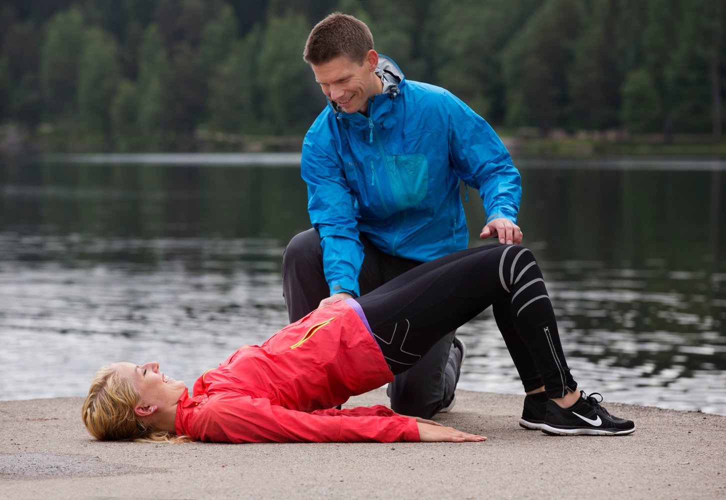 En dame ligger på en brygge mens hun hever hoften. En trener assisterer.