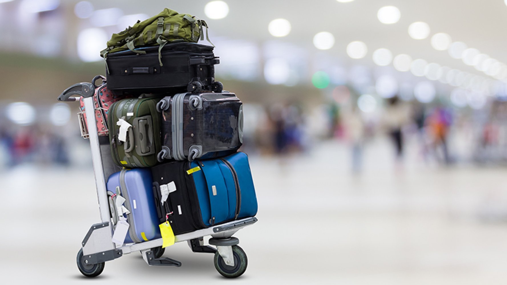 Bagasjetralle fylt med flere kofferter og vesker på en flyplass.