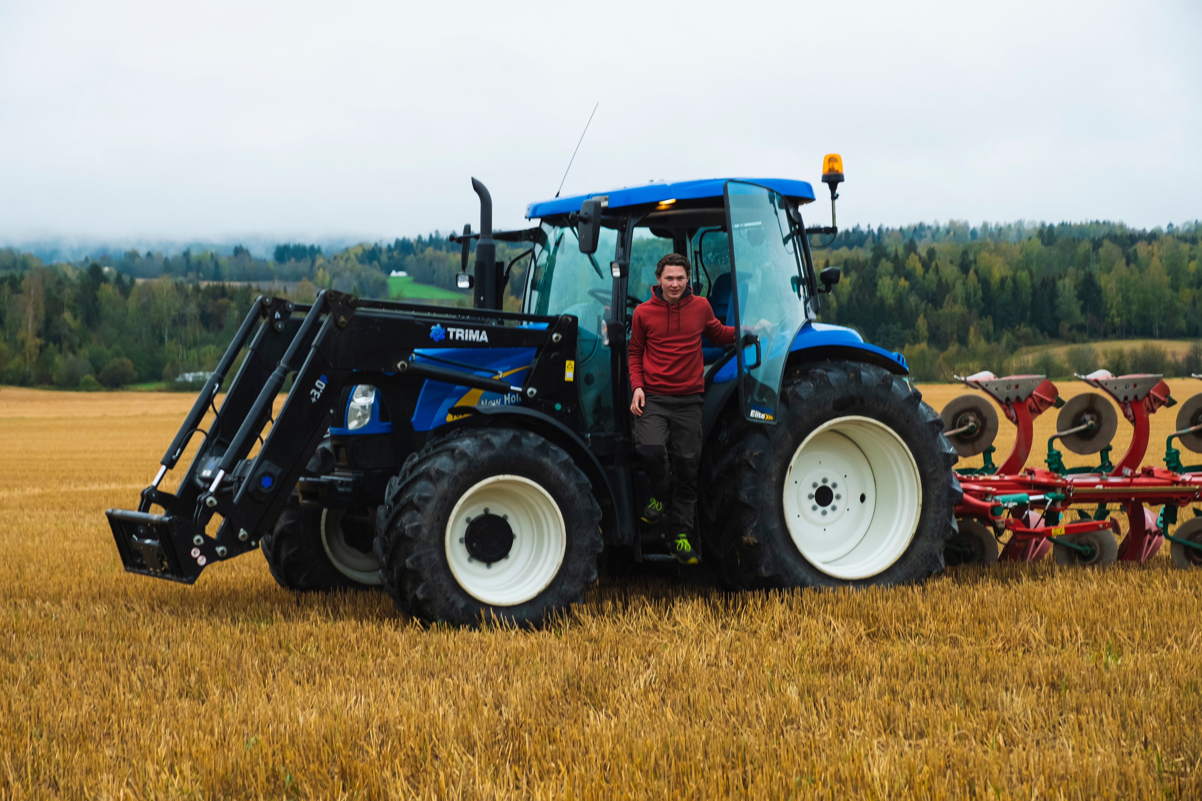 En gårdsgutt som er på vei ut av traktoren som står på åkeren.