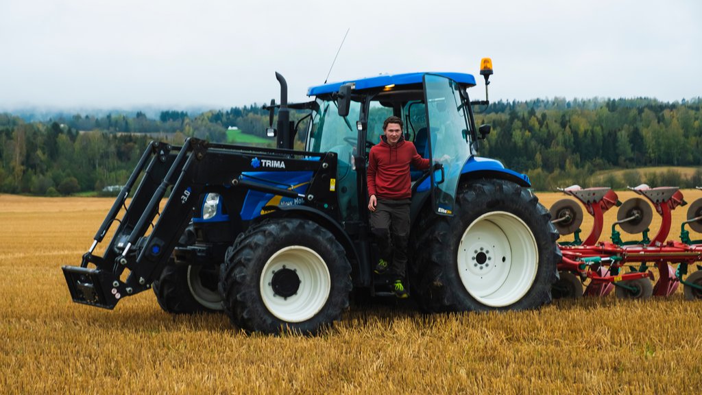 En gårdsgutt som er på vei ut av traktoren som står på åkeren.