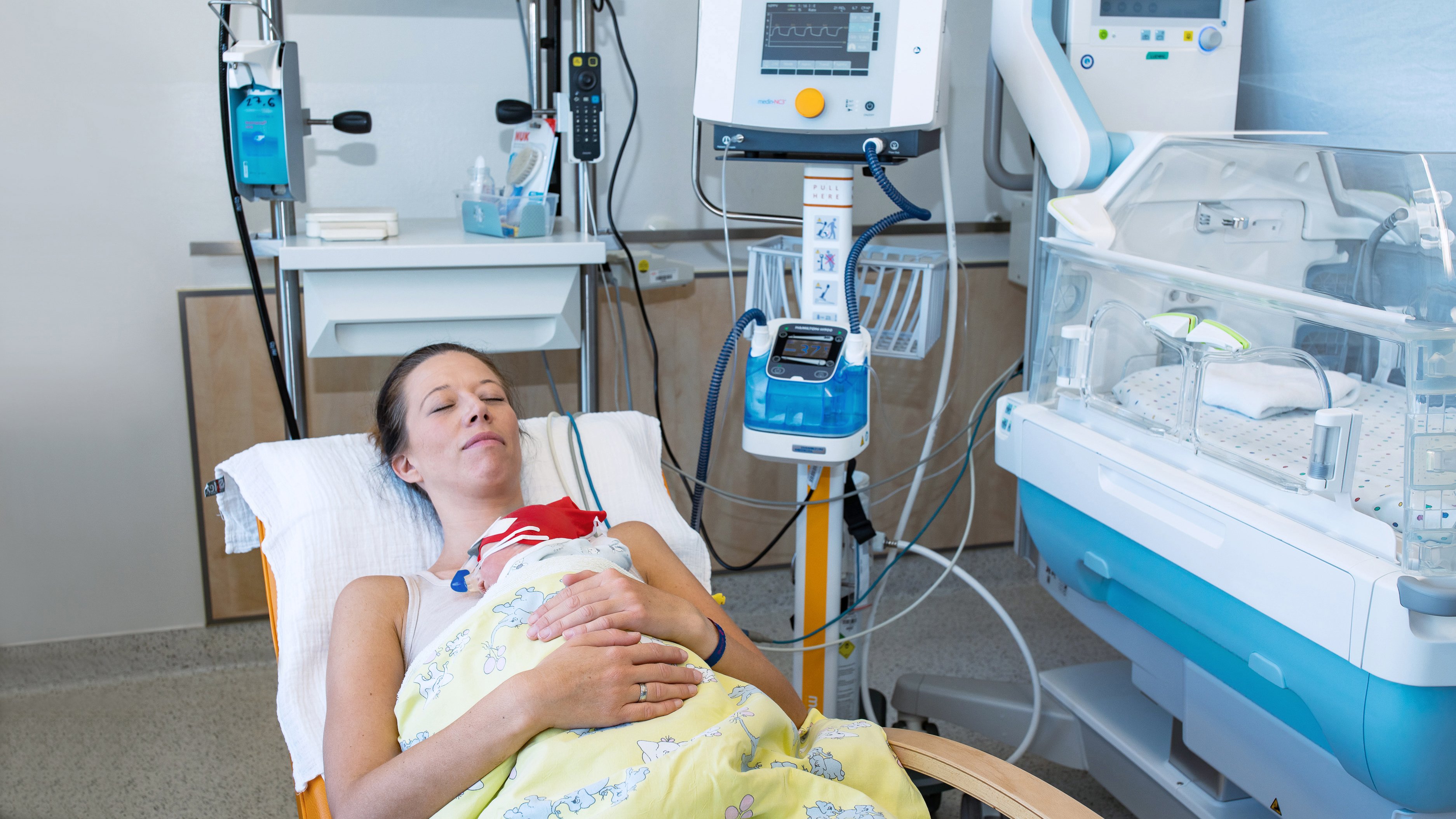 Intubated patient lies on the left side of the bed. Several people are standing next to a ventilator on the right side.