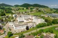 Aerial view of HUBER+SUHNER’s Herisau site in Switzerland, surrounded by green hills, farmland, residential buildings and roads.