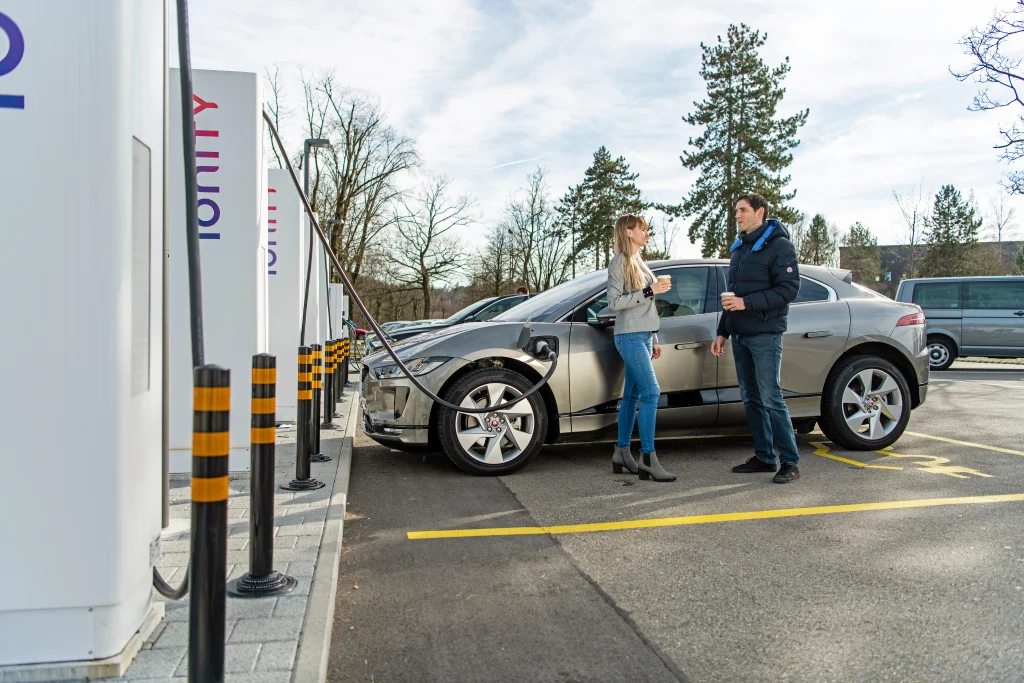 Elektrofahrzeug an einer Schnellladestation, mit zwei Personen neben dem Fahrzeug.