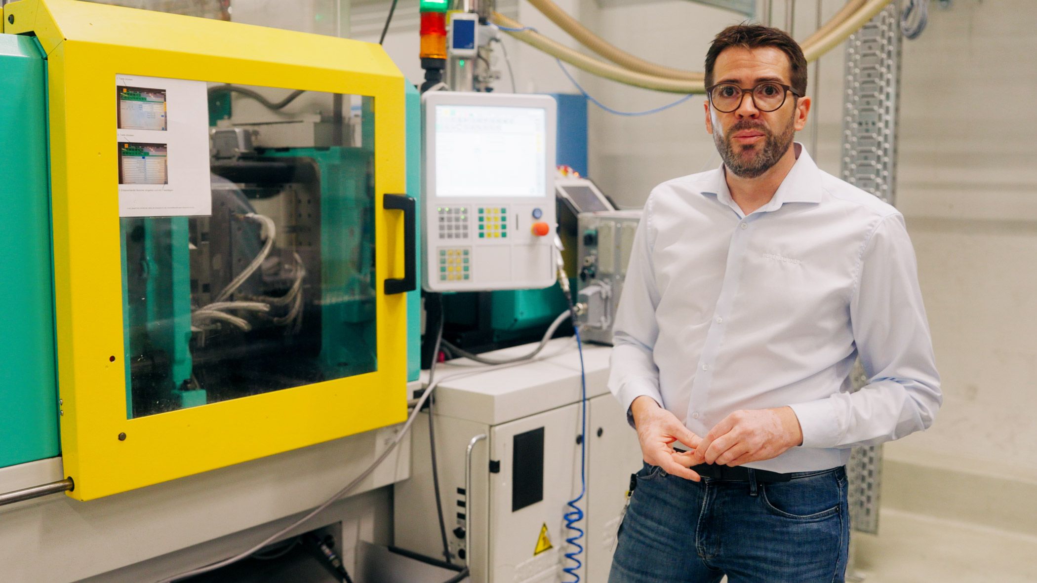 Person standing beside automated manufacturing equipment in a fiber optic production facility.