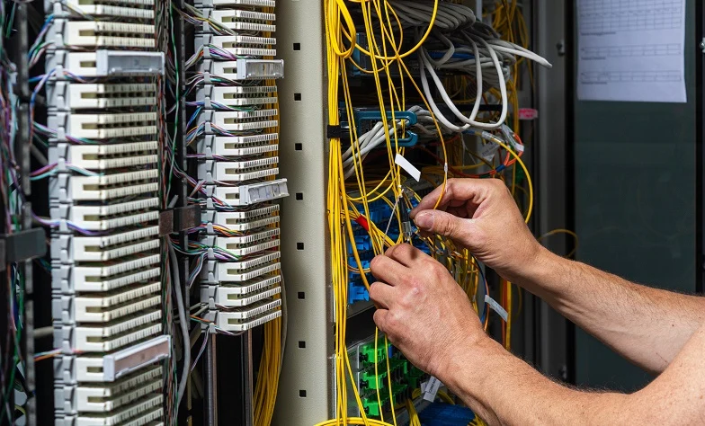 Close-up of a data rack with patch panels and bundled yellow, white, and gray cables, while hands organize and connect wiring. Close-up of a data rack with patch panels and bundled yellow, white, and gray cables, while hands organize and connect wiring.