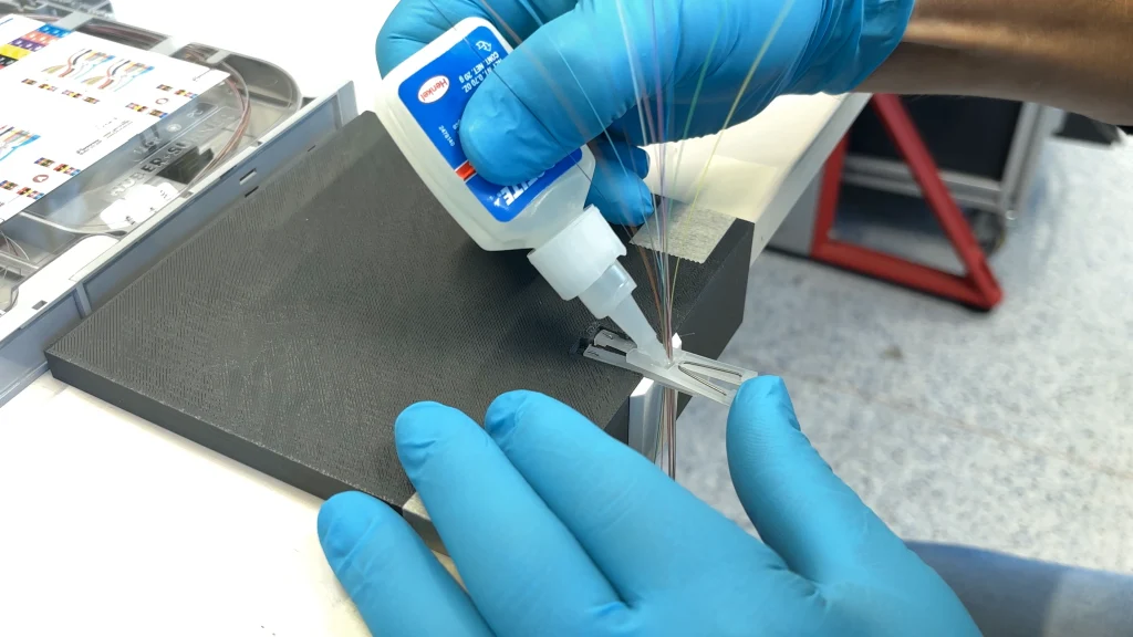 Ribbonisierungsprozess: Zwei Hände in blauen Handschuhen arbeiten mit optischen Fasern.