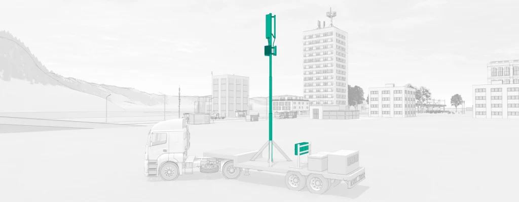 Mobile cell site mounted on a truck trailer in an open urban area, with buildings visible in the background.