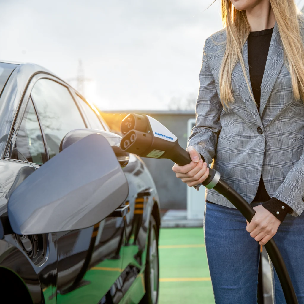 Nahaufnahme einer Frau, die neben einem Elektrofahrzeug ein Ladekabel hält.