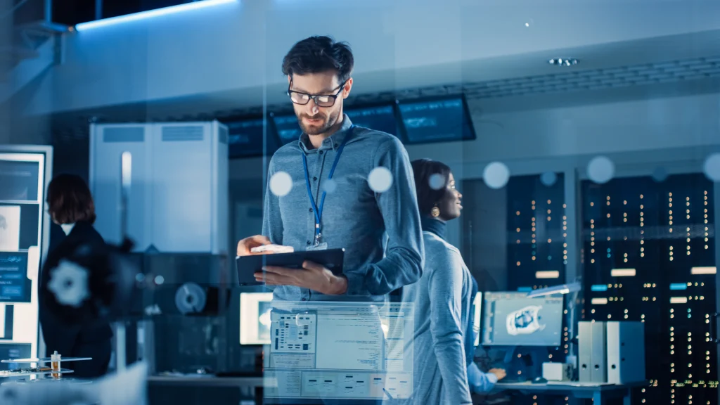 In Technology Research Facility: Chief Engineer Stands in the Middle of the Lab and Uses Tablet Computer. In Technology Research Facility: Chief Engineer Stands in the Middle of the Lab and Uses Tablet Computer.