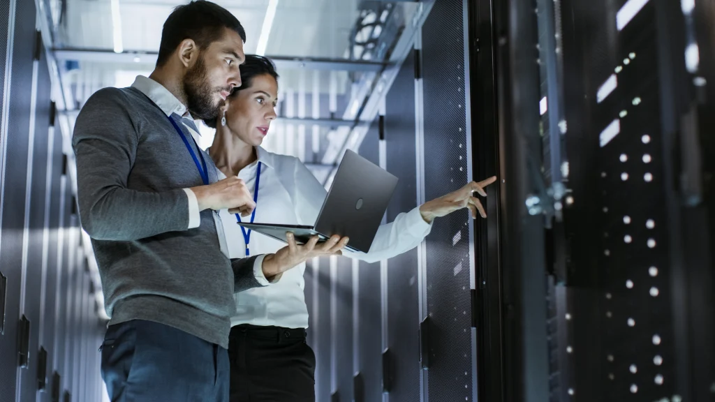 Male IT specialist holds laptop and discusses work with female server technician. They're standing in data center, rack server cabinet is open. Male IT specialist holds laptop and discusses work with female server technician. They're standing in data center, rack server cabinet is open.