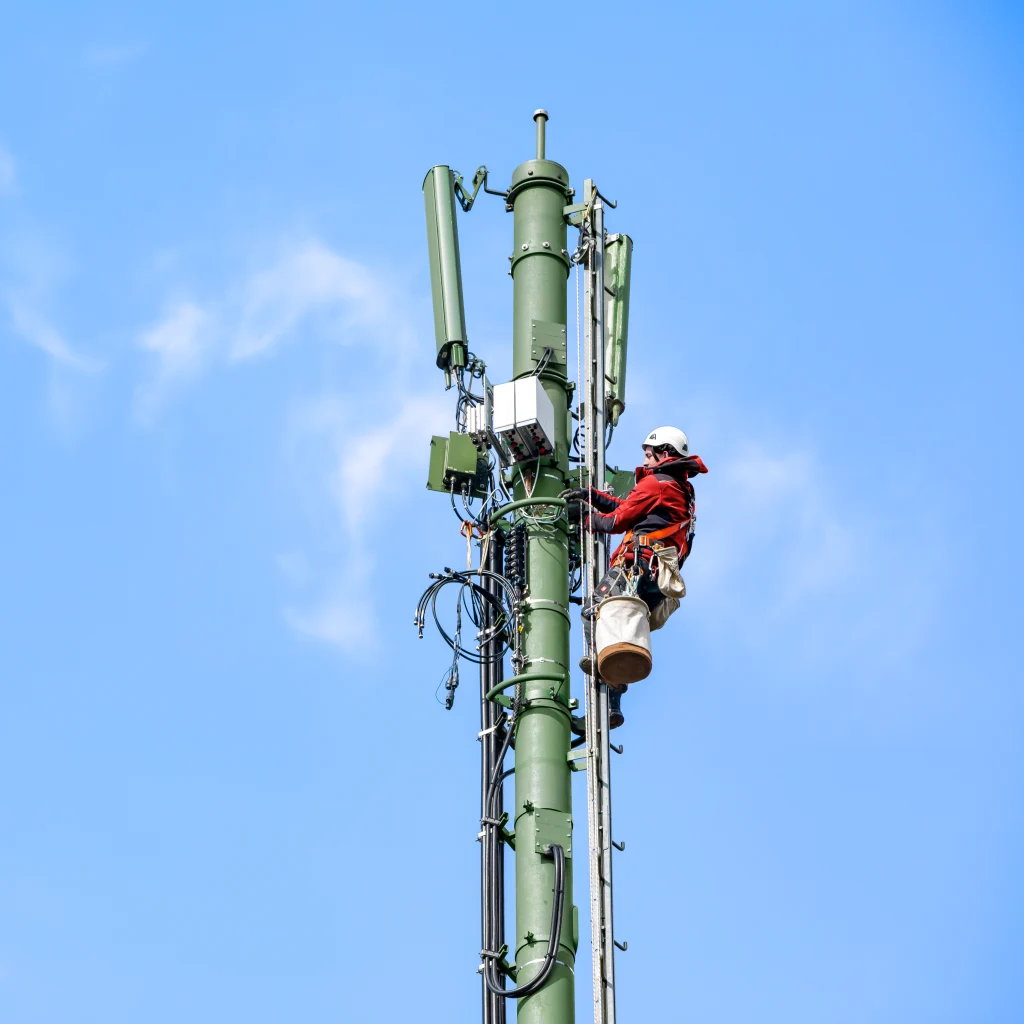 Ein Mann steht oben auf einem Mobilfunkmast vor blauem Himmel.
