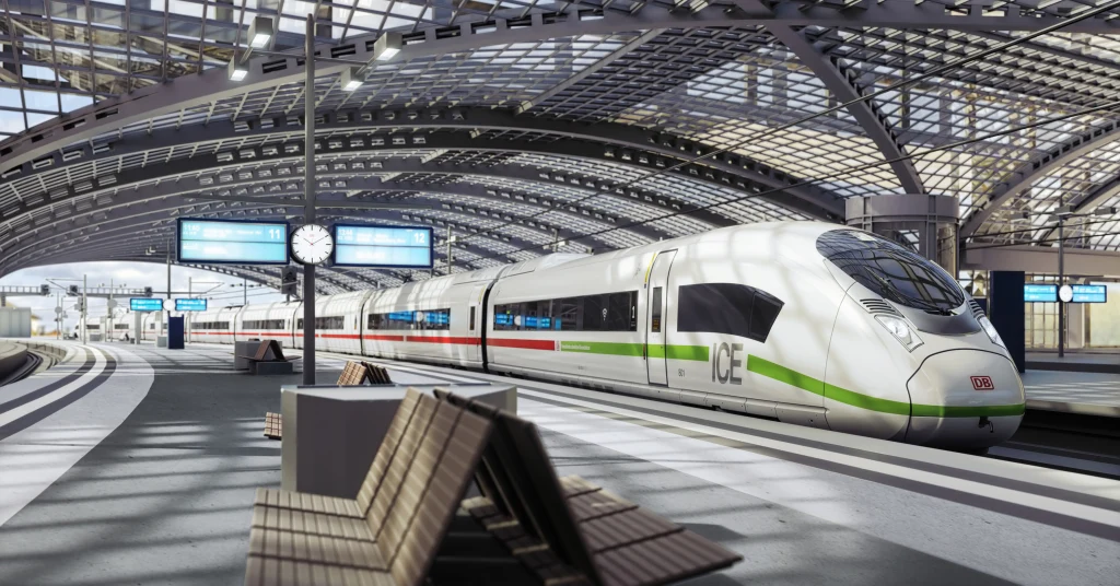 High-speed ICE train at a modern station platform under a glass roof, with digital signs, clock, and curved tracks in a bright, clean setting.