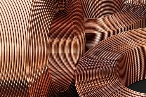 Nahaufnahme aufgerollter Kupferrohre mit glatter, reflektierender Oberfläche, eng gewickelt in kreisförmigen Rollen mit markanter Metallstruktur. Nahaufnahme aufgerollter Kupferrohre mit glatter, reflektierender Oberfläche, eng gewickelt in kreisförmigen Rollen mit markanter Metallstruktur.