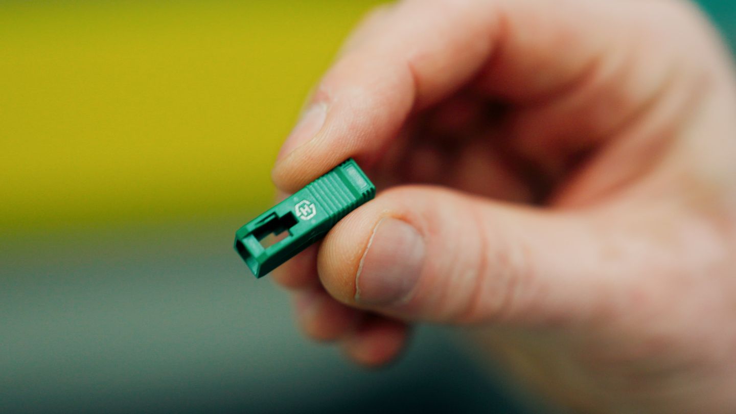 Close-up of a green fiber optic connector held between fingers for inspection.