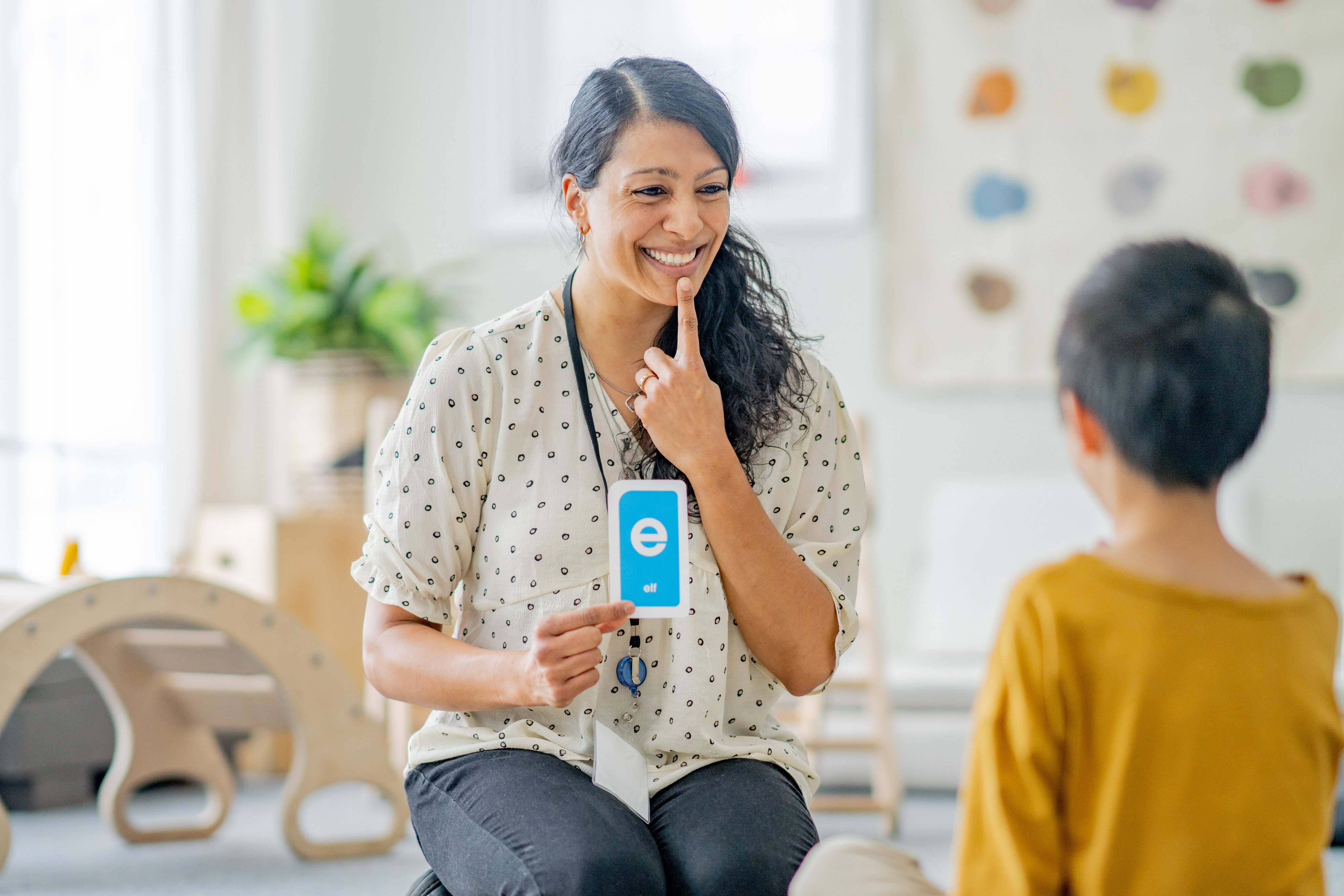 A smiling and caring speech therapist practising the E sound with a young patient.
