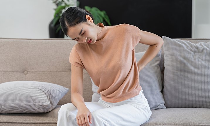 Why do I get chest or back pain when coughing Young Woman with Discomfort Seated on Sofa