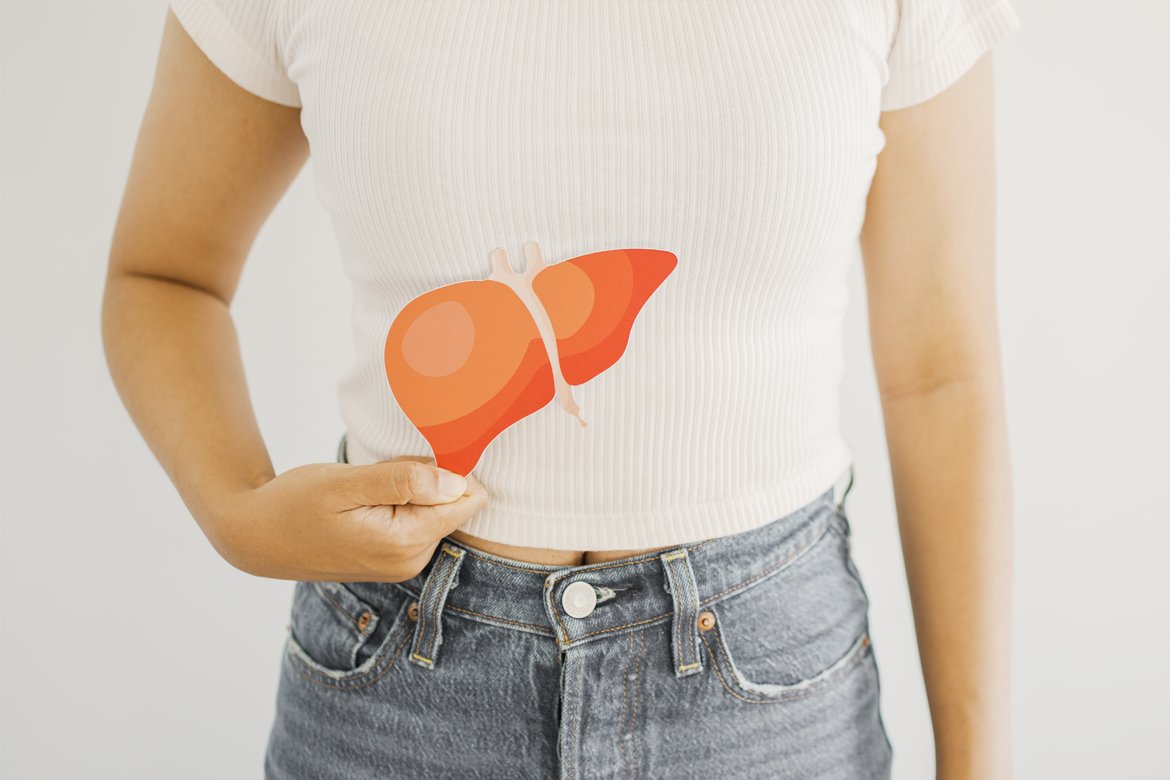 A woman holding up a paper cutout of a human liver organ to the upper right side of her torso, where her liver would be positioned in her body.