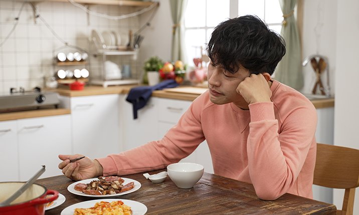 Man with black hair sits alone eating