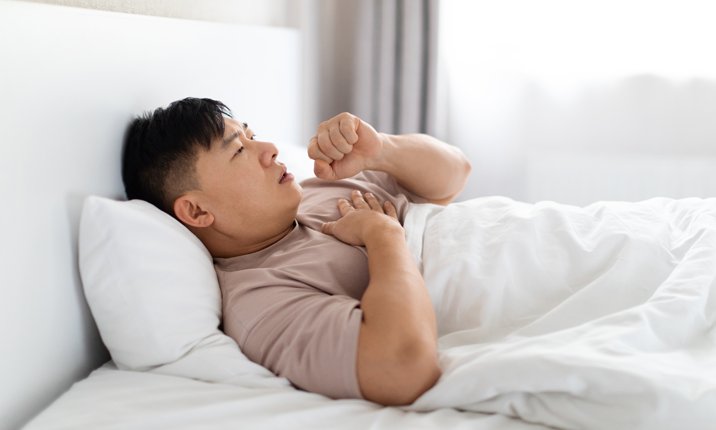 How to stop coughing at night Sick middle aged asian man smoker lying in bed, coughing