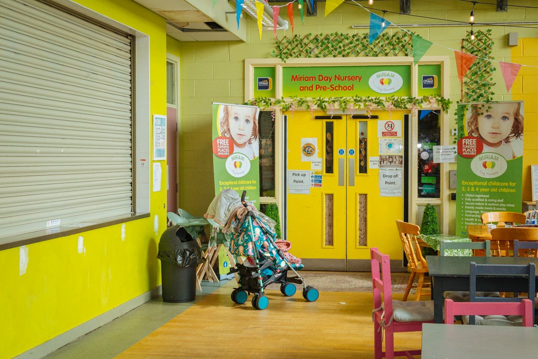 A community hall where a child's pram, laden with coats and bags is outside the entrance to a day nursery 